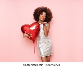 Een mooie jonge Afro-Amerikaanse vrouw met een hartvormige luchtballon op een roze achtergrond. Vrouw op Valentijnsdag. Symbool van liefde