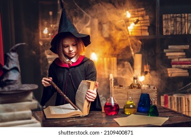 Kavkazská holčička v kostýmu čarodějnice Cosplay čte kouzelnou knihu, zatímco drží kouzelnou hůlku, kostým Halloween. Halloweenská párty.