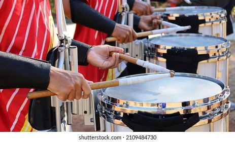 ドラムスティックとドラムを持つ手。屋外オーケストラでスネア マーチング ドラムの練習をしている赤いシャツを着た男性の列。セレクティブ フォーカス