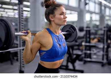 Confident fit strong woman is doing exercises with weight in modern gym, alone. caucasian female in sportive top training, lead healthy lifestyle. sports concept, fat burning and weight loss concept