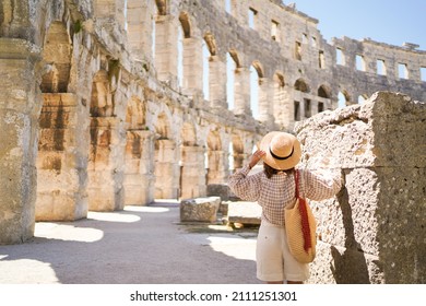 帽子をかぶった女性が立って、クロアチアのプーラにあるコロシアムを見ています。旅行のコンセプトです。若い女性は、ヨーロッパで夏のイタリアの休暇をお楽しみください。