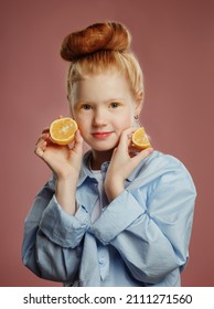 Portrait of fox hair beautiful little girl in white t-shirt and blue jacket outfit stands indoor near pink background holding orange and playing