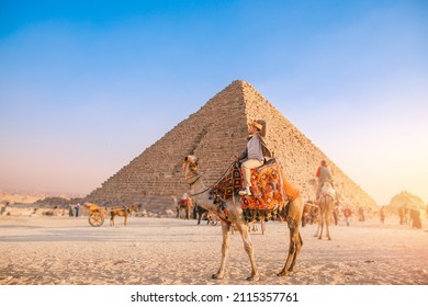 Happy Tourist man with hat riding on camel background pyramid of Egyptian Giza, sun light Cairo, Egypt.