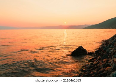 Malerischer Sonnenuntergang in goldenen orangefarbenen Farben am felsigen Strand und am späten Sommerabend am Meer