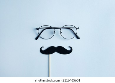 Vatertags-Feiertagskonzept. Transparente Gläser, stilvolle schwarze Papierfotokabinenstützen Schnurrbärte auf blauem Hintergrund.