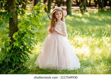 Một cô gái nhỏ trong tự nhiên trong một chiếc váy nhẹ và chiếc mũ.