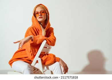 Mujer rubia de moda y segura de sí misma con sudadera naranja de moda, gafas de sol de color, posando sobre fondo blanco. Copiar, espacio vacío para texto