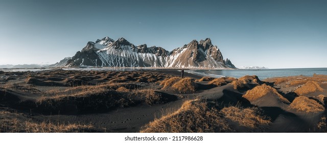 Jonge toerist staat op het strand tijdens zonsondergang en prachtige weerspiegeling van de Vestrahorn-berg op de Stokksnes-kaap in IJsland. Prachtige met sneeuw bedekte bergen. Locatie: Stokksnes-kaap