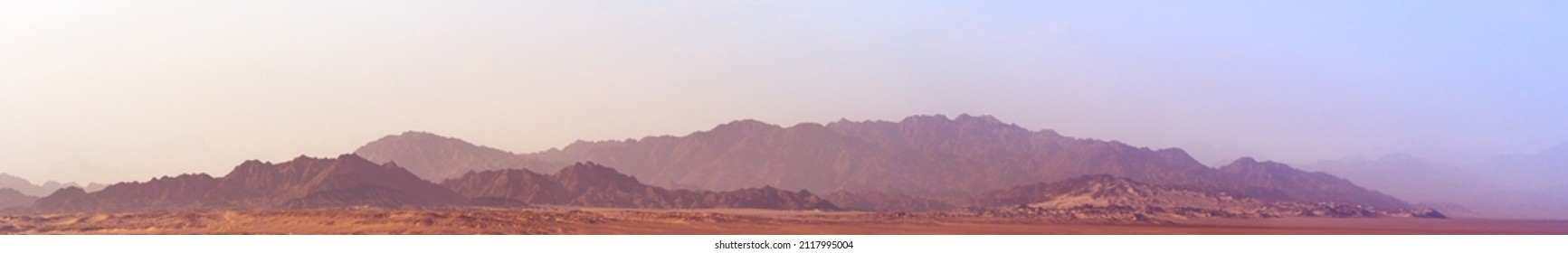 Skyline mit Berglandschaft in Pastellfarben mit violetten und rosa Farbtönen. Breites Panorama mit Bergen im Morgendunst im Nabq-Naturreservat bei Sonnenaufgang.