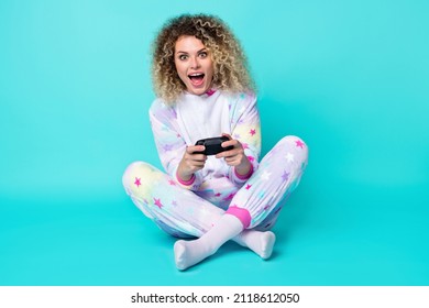 Foto in voller Größe einer coolen jungen Dame mit lockiger Frisur, die eine Playstation trägt und Pyjamasocken einzeln auf blauem Hintergrund trägt