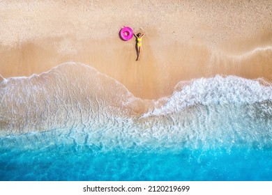 Luftaufnahme der liegenden schönen jungen Frau mit rosafarbenem Schwimmring am Sandstrand in der Nähe des Meeres mit Wellen bei Sonnenuntergang. Sommerurlaub auf der Insel Lefkada, Griechenland. Draufsicht auf schlankes Mädchen, klares azurblaues Wasser