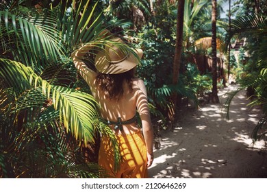 Mujer hermosa joven se encuentra a la sombra de las palmeras, vista desde atrás. Una niña camina entre la vegetación tropical en un día soleado en México, Tulum