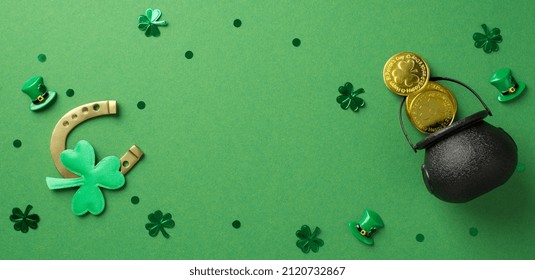 Foto da vista superior da ferradura de bronze e muitos confetes em forma de trevos, pontos, chapéus e pote preto com moedas no fundo verde isolado, espaço em branco