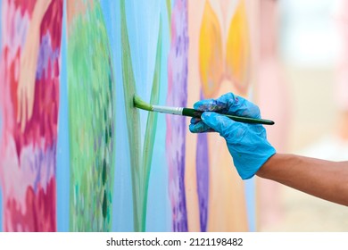 Artist's hand met penseel schilderij kleurrijke foto op canvas op outdoor kunstfestival. Vrouwenschilder in blauwe handschoenen tekent surrealistisch beeld met penseel, prachtige kunstprestaties