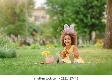 Niña negra usa orejas de conejo y recolecta huevos de Pascua en la búsqueda de huevos de Pascua en el jardín