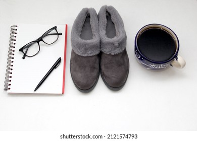 Sandal berbulu abu-abu empuk, sangat nyaman di samping buku catatan, pena, buku, gelas dan kopi untuk sejenak relaksasi dan ketenangan di samping tempat tidur