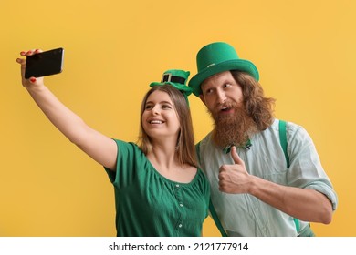 Pasangan muda yang bahagia mengambil selfie dengan latar belakang kuning. Perayaan Hari St. Patrick