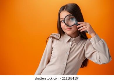 オレンジ色の背景に虫眼鏡を通して見る小さな女児。
