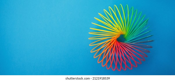 Regenboog gekleurde draad spiraal speelgoed op blauwe achtergrond. Speelgoed plastic regenboog, kleurenspiraal om te spelen. Kleurrijke spoel, banner.