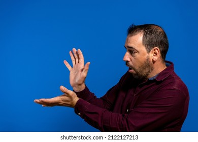Latin bearded man dressed in a purple shirt isolated on blue studio background, he is throwing a kame hame imitating Son Goku from Dragon Ball, one of his youth heroes