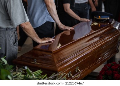 人々は埋葬前に亡くなった親戚に別れを告げるために教会にやって来て、花を持って茶色の木製の棺に触れました。その上に軍帽があります