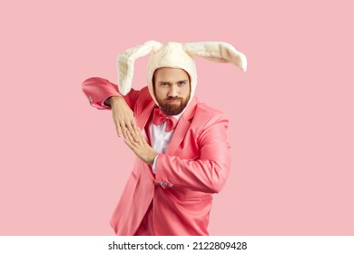 Kaninchen-Kostümparty. Fröhlicher Mann in lustigem, flauschigem Hut mit Hasenohren, der sich isoliert auf rosa Hintergrund amüsiert. Der Mann im rosafarbenen Anzug macht Tanzbewegungen mit lustigem Gesichtsausdruck. Banner.