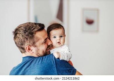 カメラを見て、困惑した女の赤ちゃんが父親の腕の中にいます。
