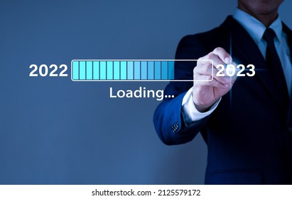 Un homme d'affaires appuie sur une barre de téléchargement virtuelle avec un indicateur de progression de chargement le soir du Nouvel An, transformant l'année 2022 en 2023.
