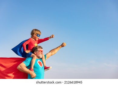 Pria senior superhero dan anak bermain di luar ruangan. Kakek pahlawan super dan anak laki-laki bersenang-senang bersama dengan latar belakang langit biru musim panas. Konsep liburan keluarga. Selamat Hari Ayah