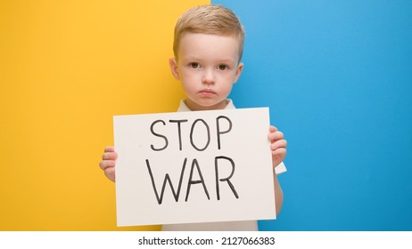 Portret serieuze blonde 4-jarige jongen die protesteert tegen oorlog heft spandoek op met inscriptie Stop War bij de blauwgele vlag van het land Oekraïne. Oproep om oorlog te stoppen, kind tegen oorlog, crisis in Oekraïne.