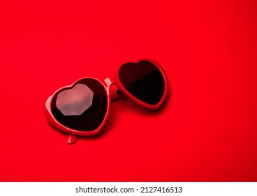 Gafas de sol en forma de corazón rojo sobre fondo rojo vibrante. Día de San Valentín, Purim, amor, concepto de viaje, pancarta, postal con espacio para copiar.