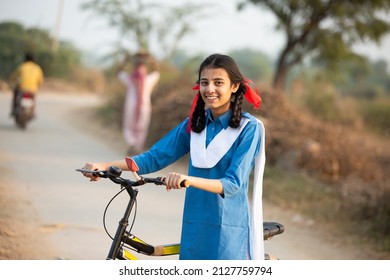 村の通りで自転車で立っている青い学校の制服を着て幸せな若い田舎のインドの女の子の肖像画。