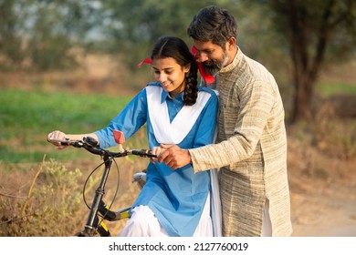 Rural indian father teaching his daughter to ride bicycle at village, young girl wearing school uniform learning cycling. closeup