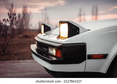 ポップアップ ヘッドライトと白い古い日本の 1980 年代の車。バック グラウンドでぼやけた田園地帯