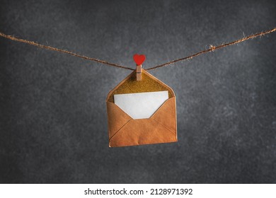 Umschlag mit Nachricht, die am Seil mit Wäscheklammer in Form von Herzen auf grauem Hintergrund hängt. Valentinstag. Platz kopieren