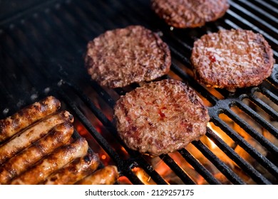 Grillen von rauchigem Hamburgerfleisch für Burger. Auf offenem Feuer auf dem Grill braten - bbq.Burger und Würstchen, die über Flammen auf dem Grill kochen.