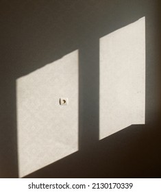 Sun flares are polygonal in shape. Sunlight from the window falls on light wall with ornament and power socket. Abstract background with light and shaded areas. Space for copy. Vertical photo.
