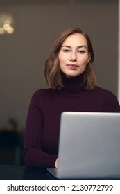 Portræt af smuk brunette forretningskvinde i rullekrave foran sin bærbare computer, ser på kameraet meget selvsikker og tilfreds. Koncept: professionel forretningskvinde