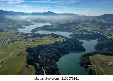 スイスのフリブー​​ル州にある湖、グリュイエール湖の空撮。湖はこの地域の丘を曲がりくねって流れ、木々の層に囲まれています。高品質の写真