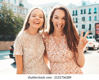 Two young beautiful smiling hipster female in trendy summer dresses.Sexy carefree women posing in the street. Positive pure models having fun at sunset, hugging and going crazy. Show peace sign