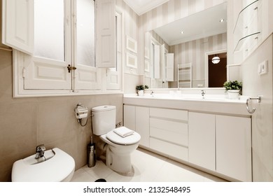 One-piece white porcelain washbasin with two bowls on a white wooden cabinet with a square frameless mirror and a white heated towel rail next to the door