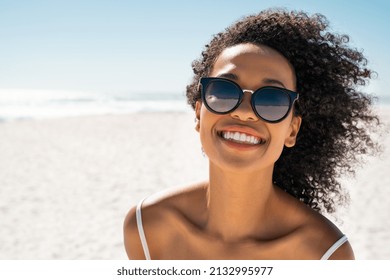 Portrait of smiling black woman wearing fashion sunglasses at the beach with copy space. Pretty african american girl wearing specs at the seaside during summer vacation. Beautiful young woman at sea 