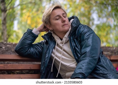 một cô gái với mái tóc vàng ngắn ngồi trên ghế dài trong công viên trong mùa thu ấm áp với vẻ trầm ngâm.