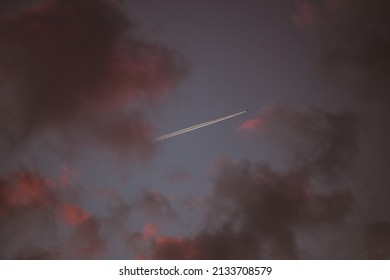 paarse wolken in donkere avondlucht en vliegtuig met witte rookspoor ver weg
