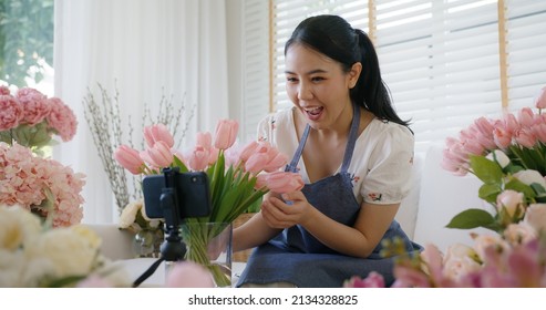 Asia girl vlogger influencer or SME owner people smile work on home video camera selfie shoot filming for live sell show happy talk on mobile VoIP app. Remote sale product at modern florist gift shop.