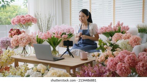 Asia girl vlogger influencer or SME owner people smile work on home video camera selfie shoot filming for live sell show happy talk on mobile VoIP app. Remote sale product at modern florist gift shop.