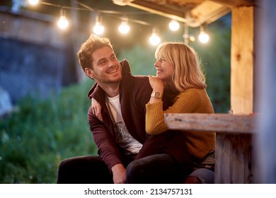 Lächelndes junges Paar, das sich auf einem Holzhaus auf der Terrasse in der Natur entspannt.