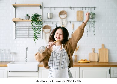 Asiatisk ung kvinde danser i køkkenrummet. Hun er glad og afslappende i fritiden i weekenden