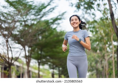 Gelukkige slanke vrouw die sportkleding draagt ​​die in de stad bij zonsopgang jogt. Jonge mooie Aziatische vrouw in sportbeha die buiten loopt. Trainingsoefening in de ochtend. Gezond en actief levensstijlconcept.
