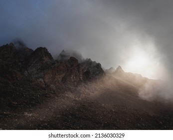 Soft focus. Darkness minimalist landscape with big mountain rocks above low clouds with sun rays. Atmospheric ghostly minimalism with large mountain tops in cloudy sky.